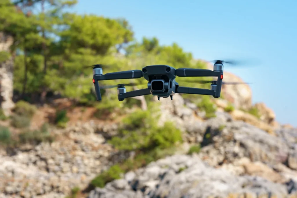 dron compacto con cámara volando frente a un paisaje rocoso con árboles