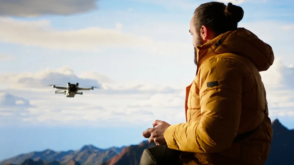 persona controlando un dron volando a distancia sobre un paisaje de montañas