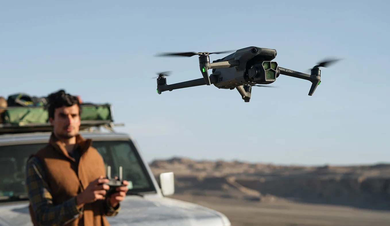 Imagen del DJI Mavic 3 Pro en primer plano y de fondo una persona piloteando junto a un auto