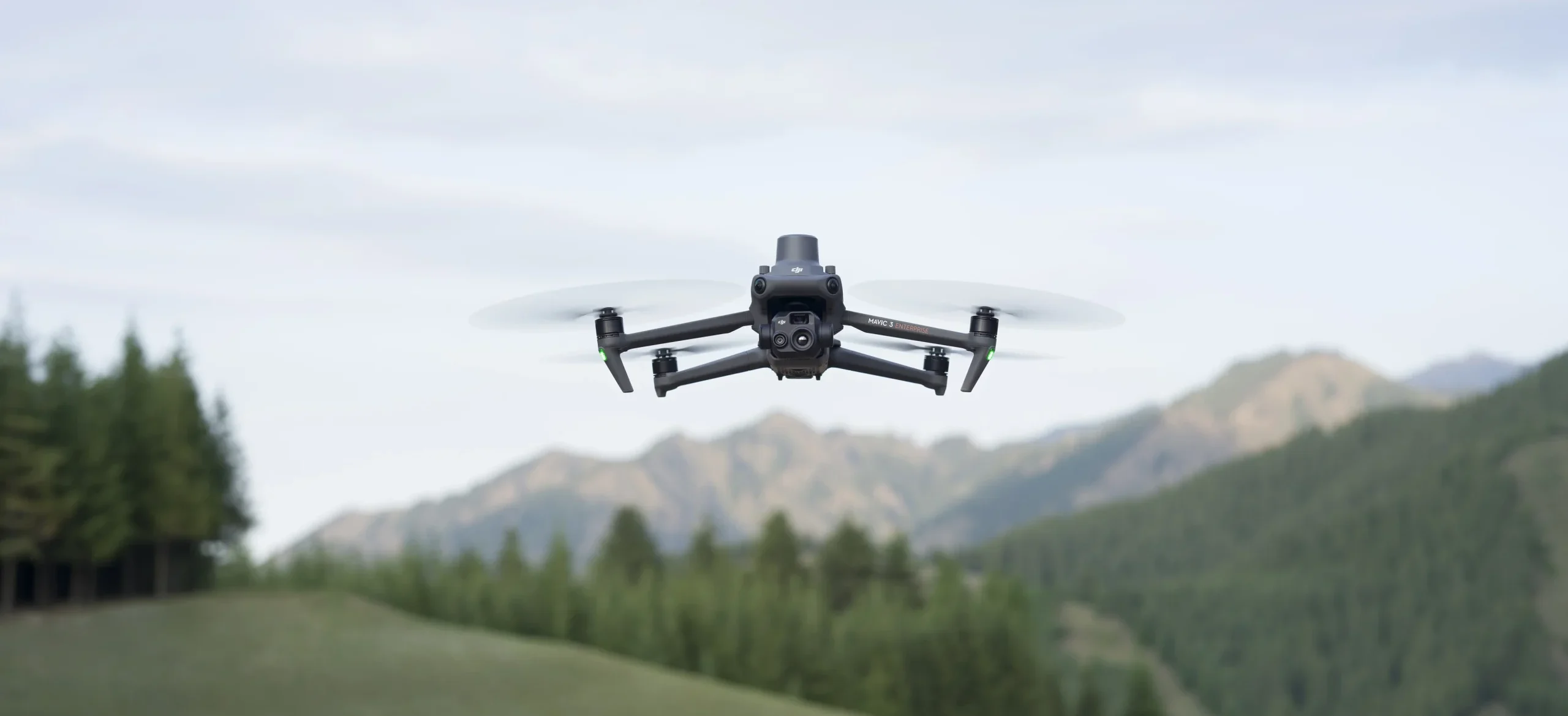 Imagen del DJI Mavic 3 Thermal y en la parte de atras un campo con montañas y bosque 