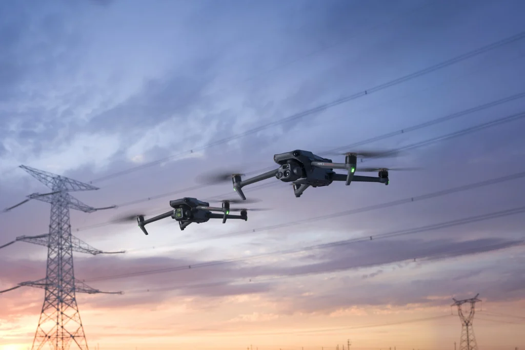 Imagen de un atardecer y en primer plano dos drones Mavic, uno 3E y otro 3T