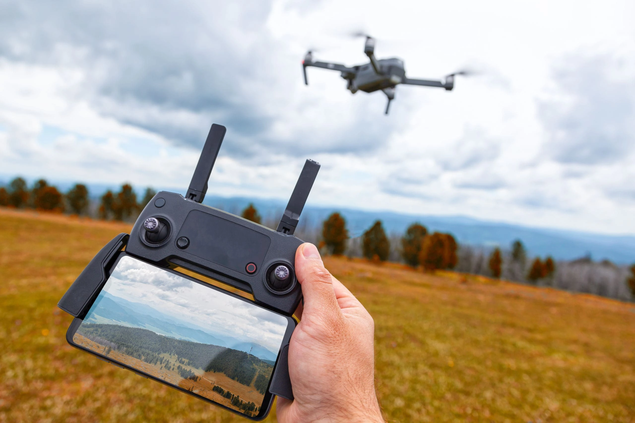 imagen de un dron, de fondo un campo con el cielo y desenfocado una persona piloteando 