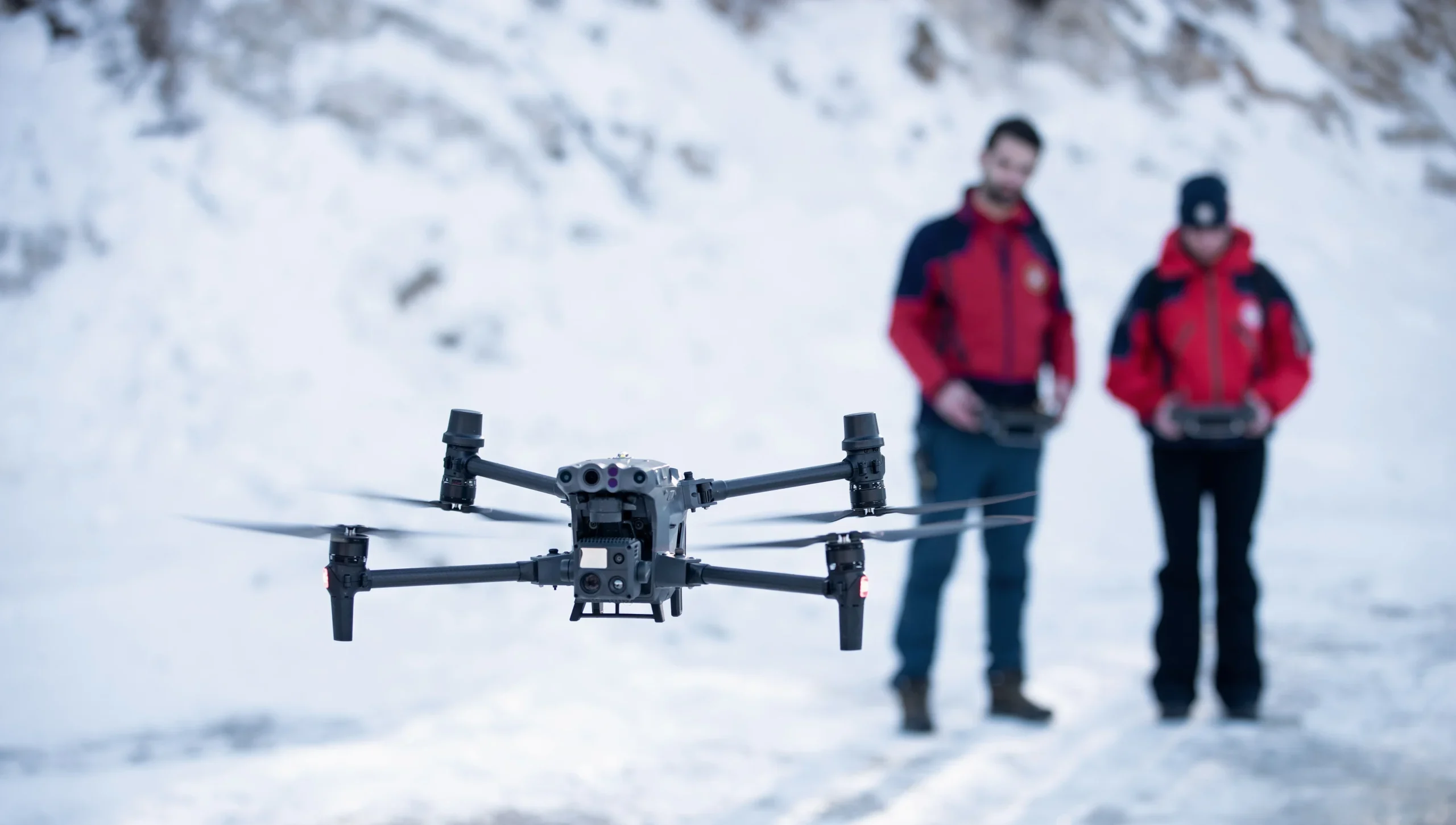 Primer plano del M30T y segundo plano de dos personas piloteando rodeados de nieve